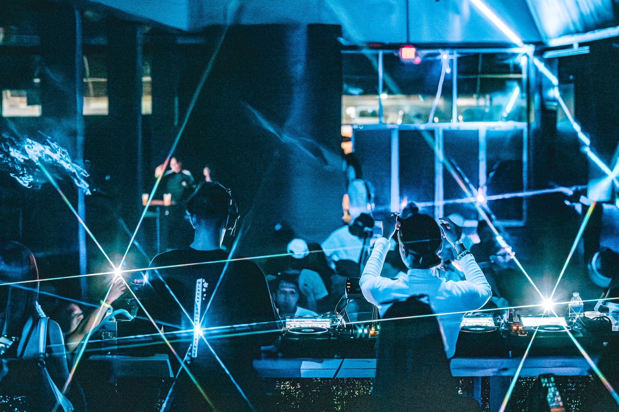 Packed main room swept by green laser beams beneath a mirror ball